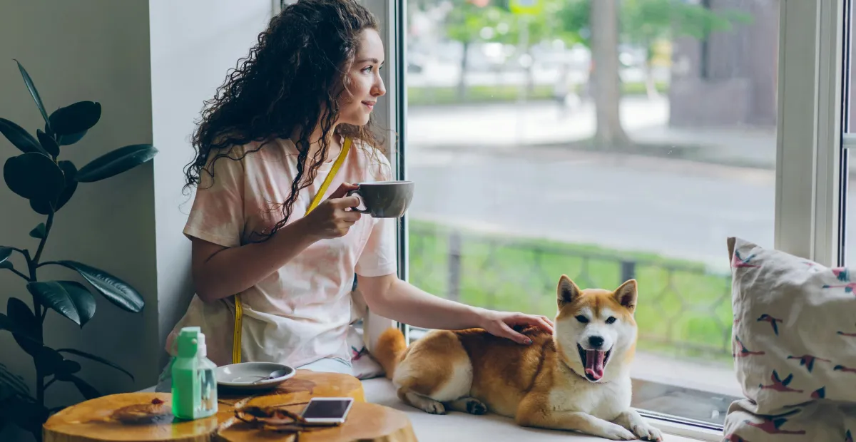 woman sitting in a cafe drinking coffee with a dog next to her